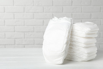 Baby diapers on wooden table against white brick wall. Space for text