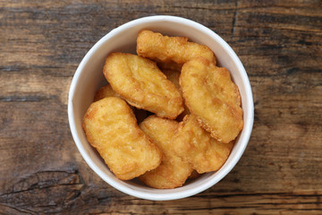 Bucket with tasty chicken nuggets on wooden table, top view