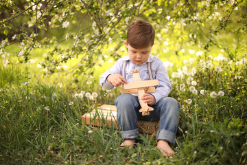Fototapeta na wymiar Little cute blond boy playing with a wooden plane in the summer park on the grass on a sunny day