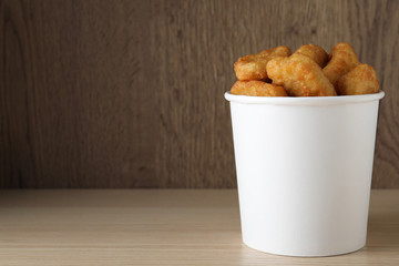 Bucket with tasty chicken nuggets on wooden table. Space for text