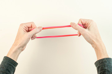 Red rubber band being stretched from two sides by woman.