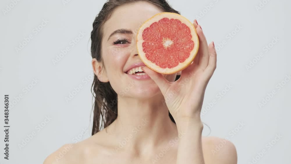 Canvas Prints A smiling young half-naked woman with wet hair is posing while holding a grapefruit isolated over a light blue background in studio