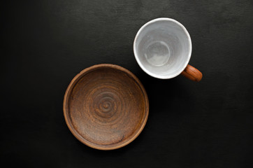 Empty brown ceramic tableware cup and plate on a black slate background. The concept of food and its absence.