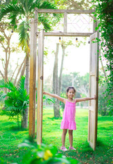 Obraz premium little asian girl standing at a big wooden door to the garden