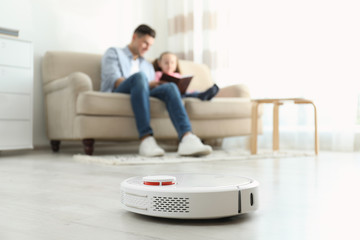 Man and his daughter resting while robotic vacuum cleaner doing its work at home