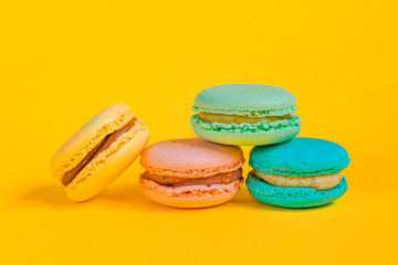 Sweet almond colorful unicorn pink blue yellow green macaron or macaroon dessert cake isolated on trendy yellow modern fashion background. French sweet cookie. Minimal food bakery concept Copy space