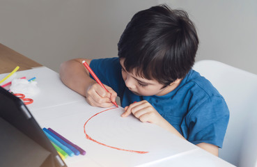 Kid red pen colouring rainbow on paper,Child using digital tablet for homework online lesson,Boy enjoy art activity at home, self-isolation, online education, home schooling, distance learning concept