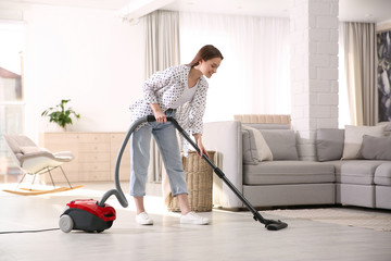 Young woman using vacuum cleaner at home - obrazy, fototapety, plakaty
