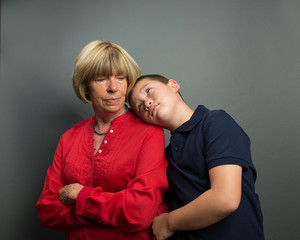 Preteen boy leaning head on shoulder of mother as if wanting to receive forgiveness for wrongdoing.