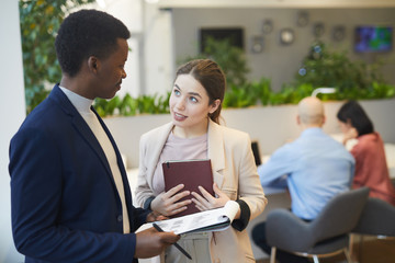 Waist up portrait of young eager businesswoman talking to manager while discussing work project in office, copy space