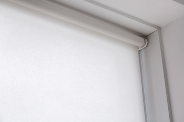 white rolled textile blinds on the window in a room, object of protection against sunlight close up...