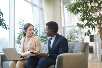 Portrait of successful African businessman talking to female partner while working sitting comfortable chair at office building hall, copy space