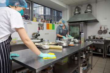 Woman in protective mask and gloves disinfecting kitchen table