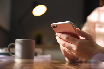 Woman with smartphone at table indoors, closeup on hands