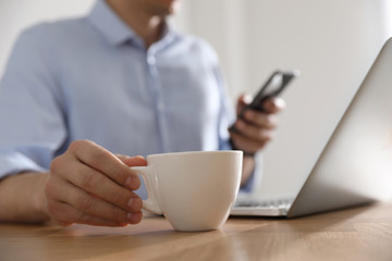 Man with cup of coffee at table indoors, closeup