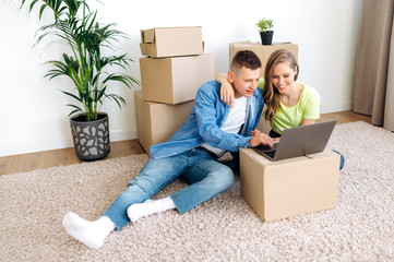 A young couple in love moved to their own home. They shopping online in their new housing using a laptop, they buy furniture and various household appliances for home