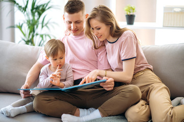 Family leisure at home. Young parents read a children's book with their beloved little son, sitting...