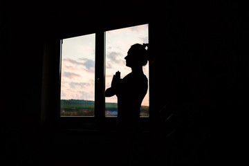 woman silhouette in yoga pose by window at sunet