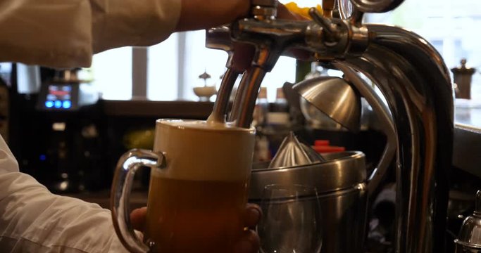 Barman hand at beer tap pouring a draught lager beer serving in a restaurant or pub.