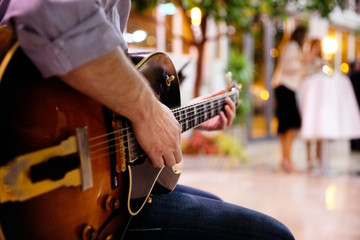 Detail of the hand of a young man playing an electro-acoustic rock guitar outdoors.