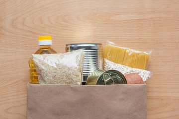 Pasta, rice, oatmeal, oil, potatoes and canned food in paper bag on wooden background top view. Food grocery delivery, donation or stock provision concept. Copy space.