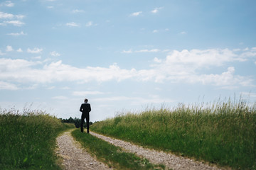 photo of a man standing on a way between two fields