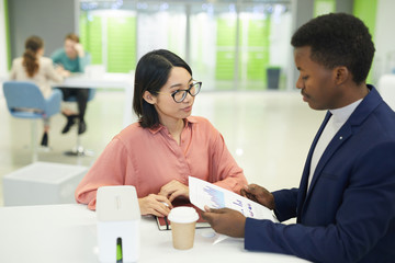 Portrait young Asian businesswoman discussing work documents with colleague while sitting at table during lunch break in office