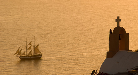 A Tall Ship sails past a church off the coast of Oia, Santorini, Greece.