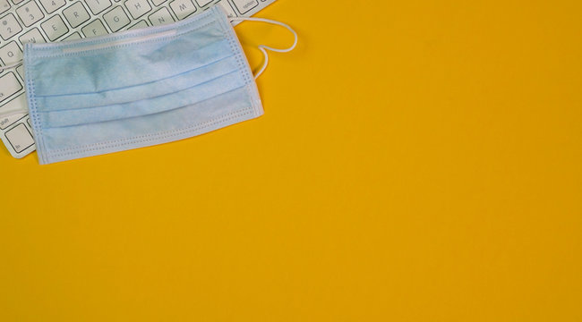 Medical face mask on top of keyboard. Yellow background. Top view.