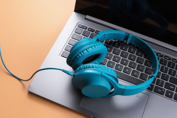 Photo of stylish modern computer or notebook and blue cyan headphones over beige background. Close-up.