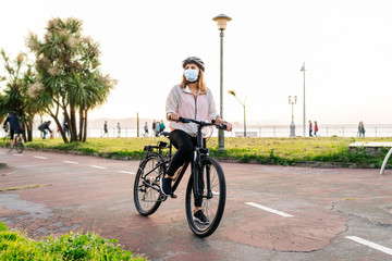 Portrait of a woman with protective safety mask on her face riding a bike on a bike path in the city on a sunny day.