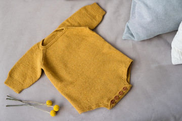 on a gray sofa there is a knitted bodysuit for the baby, mustard-colored clothes made of wool, warm winter clothes for the child for the winter