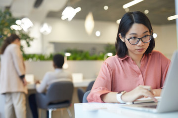 Portrait of young Asian woman using laptop while studying in cafe, copy space