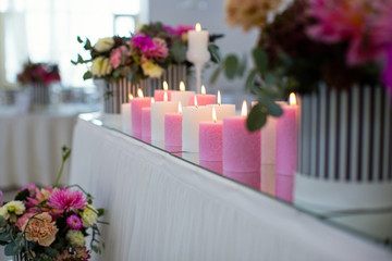 candles are burning ,white and pink candles stand on the table of the youth, festive decor of the hall, table decoration for the wedding, striped boxes with fresh flowers,