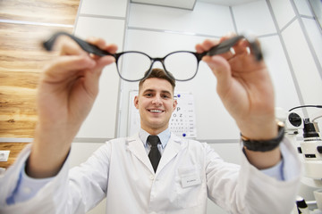 POV shot of smiling optometrist putting on glasses on unrecognizable patient during vision test in modern clinic, copy space