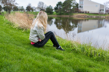 Woman/girl sitting on a grass in front of water of a lake