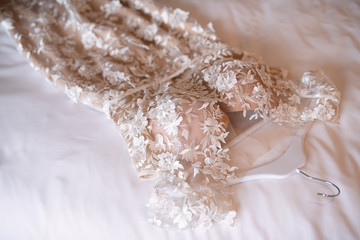 outfit of the bride ,the wedding dress lies on the bed, white bedding, the bride?s room, the morning before the wedding, the dress is decorated with fabric flowers,