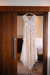 a wedding dress on a hanger hangs in the doorway, the morning of a sissy, the bride's outfit before the wedding, the dress is decorated with fabric flowers