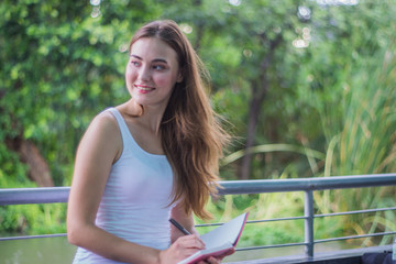 Beautiful young woman writing into her diary, in the garden
