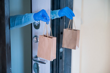 Close-up of a courier's hands in gloves with a paper bag in their hands at the front door. Quarantine delivery service.