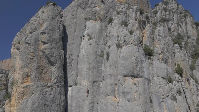 AERIAL DRONE BACKWARD SHOT DISCOVERING 2 PERSONS CLIMBING A MOUNTAIN WALL
