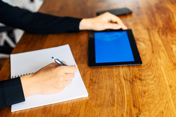 Online study concept, online classes. Close-up a hand of woman is writing abstract in notebook, a digital tablet with blank screen on the background