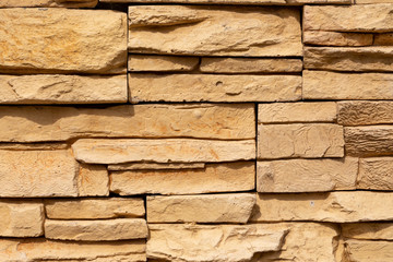 Texture of the yellow surface of a slate stone. Blocks of artificial finishing stone for wall decoration. Rough stone background