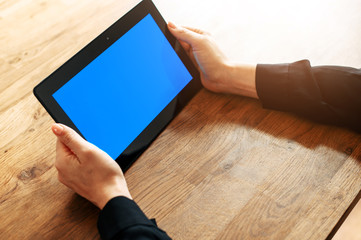 Close-up female hands hold a digital tablet with a blank screen on a wooden background. Copy space for text, mockup
