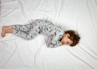 Top view of a small boy sleeping on a white bed in his pajamas. Calm posture of the fetus. The concept of sleeping positions