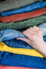 Female hand picks jeans from a stack of neatly folded trousers in bright colors.