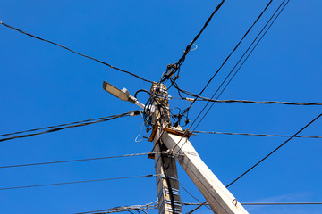A concrete electric pole with a street lamp and lots of wires against a blue sky