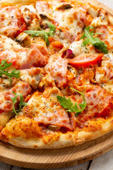 Tasty pizza with ham, mushrooms, tomatoes and arugula on wooden cutting board on white background.