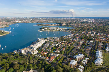 Fototapeta premium The Sydney suburb of Canada Bay and hen and chicken bay with back burning bush fire smoke coming from the Royal National Park in the South.