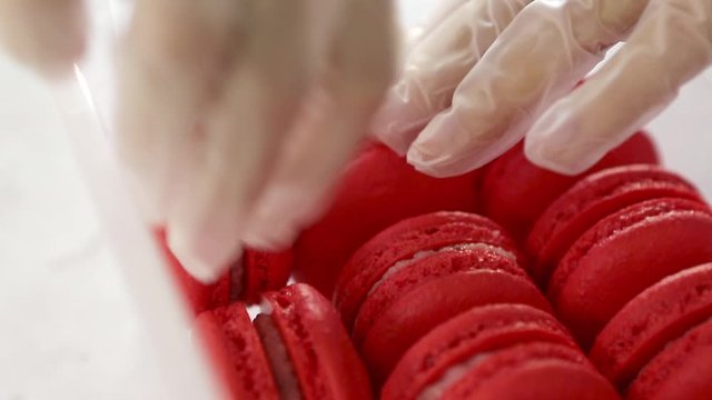  Chefs hands packaging fresh baked red strawberry macaroon into container